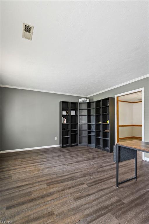 unfurnished living room featuring baseboards, visible vents, wood finished floors, and ornamental molding