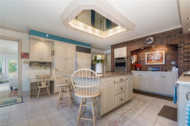 8429 Denwood Rd, Franktown, VA 23354 - kitchen with light tile patterned floors, crown molding, a center island with sink, brick wall, and a breakfast bar
