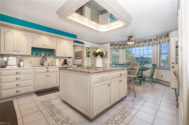 kitchen with light tile patterned floors, ceiling fan, a kitchen island, and sink