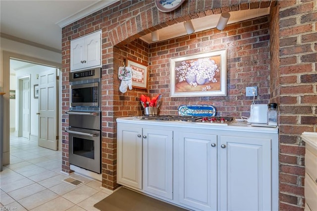 kitchen with white cabinetry, brick wall, and light tile patterned floors