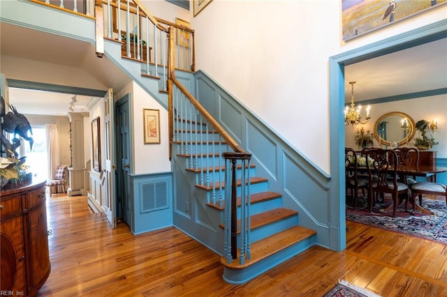 staircase with ornamental molding, wood-type flooring, and a chandelier