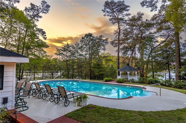 pool at dusk with a patio area and a gazebo