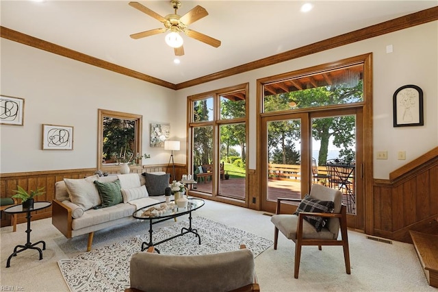 living room featuring wood walls, ornamental molding, light colored carpet, and ceiling fan