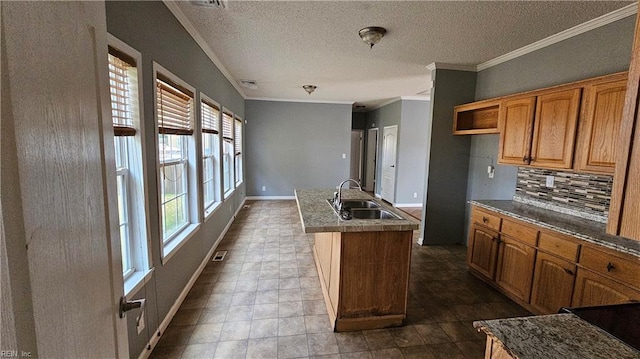 kitchen featuring crown molding, sink, decorative backsplash, a textured ceiling, and an island with sink