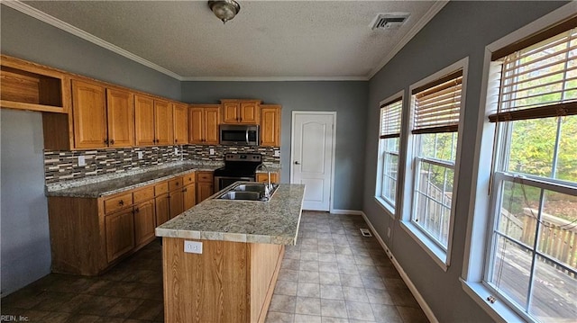 kitchen featuring appliances with stainless steel finishes, tasteful backsplash, a textured ceiling, sink, and an island with sink