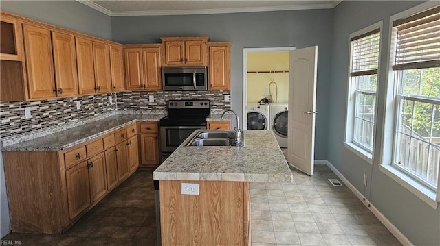 kitchen featuring a center island with sink, sink, decorative backsplash, stainless steel appliances, and washing machine and clothes dryer