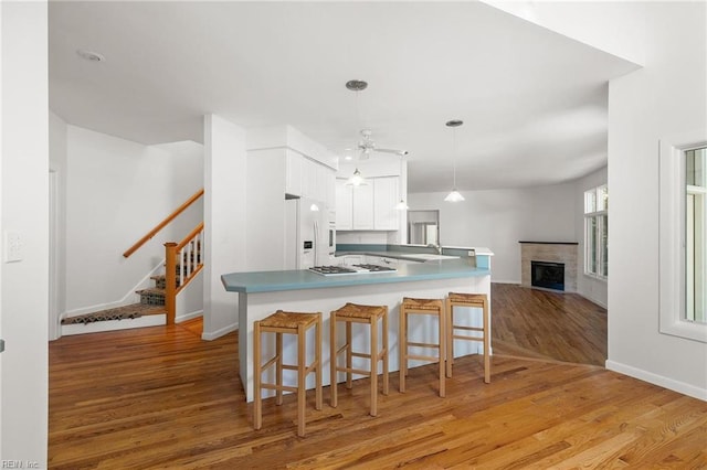 kitchen featuring light hardwood / wood-style flooring, decorative light fixtures, white refrigerator with ice dispenser, white cabinetry, and kitchen peninsula