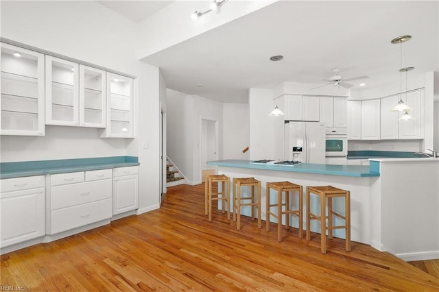 kitchen featuring white cabinets, light hardwood / wood-style flooring, white appliances, ceiling fan, and a breakfast bar area