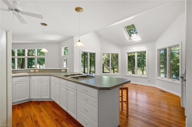 kitchen featuring a breakfast bar area, stainless steel gas cooktop, hardwood / wood-style flooring, ceiling fan, and white cabinets