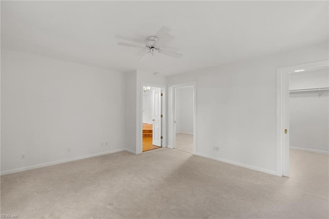 unfurnished bedroom featuring a spacious closet, a closet, ensuite bath, light colored carpet, and ceiling fan