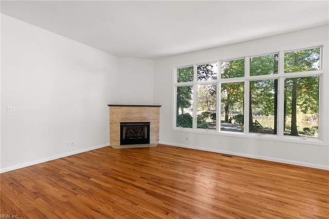 unfurnished living room featuring a tile fireplace, hardwood / wood-style flooring, and a healthy amount of sunlight