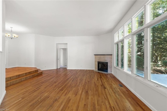 unfurnished living room featuring a tiled fireplace, wood-type flooring, and a notable chandelier