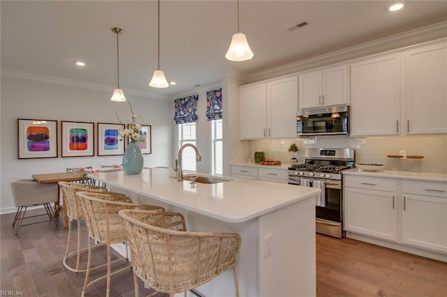 kitchen with stainless steel appliances, white cabinetry, sink, and a center island with sink