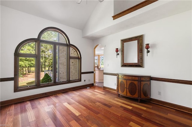 unfurnished room with a wealth of natural light, baseboards, arched walkways, and wood finished floors