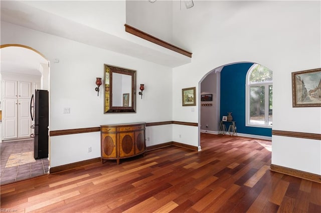 unfurnished room featuring arched walkways, a high ceiling, baseboards, and wood finished floors