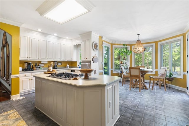 kitchen featuring a kitchen island, stainless steel gas stovetop, decorative light fixtures, and white cabinets