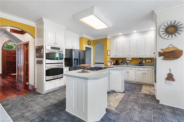 kitchen with arched walkways, white cabinets, appliances with stainless steel finishes, and a center island