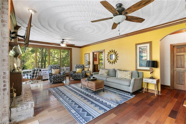 living room featuring ceiling fan, baseboards, ornamental molding, wood finished floors, and arched walkways