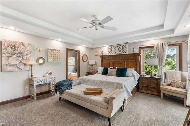 bedroom with a ceiling fan, baseboards, light carpet, a raised ceiling, and connected bathroom