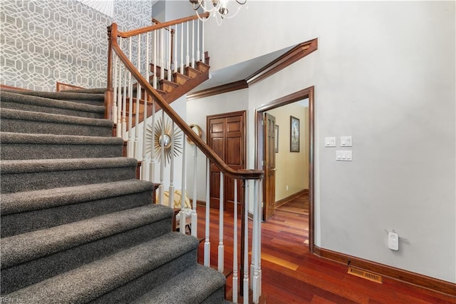 staircase with visible vents, wood finished floors, crown molding, baseboards, and a towering ceiling