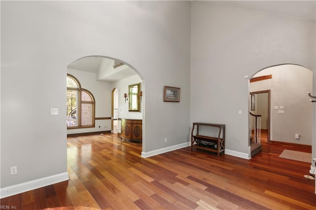 interior space with arched walkways, a towering ceiling, baseboards, and wood finished floors