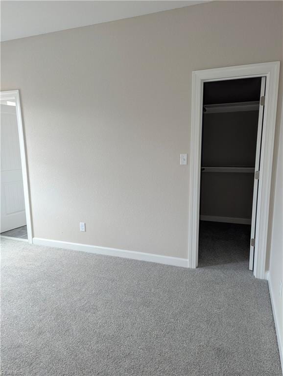 unfurnished bedroom with a spacious closet, carpet flooring, baseboards, and a closet