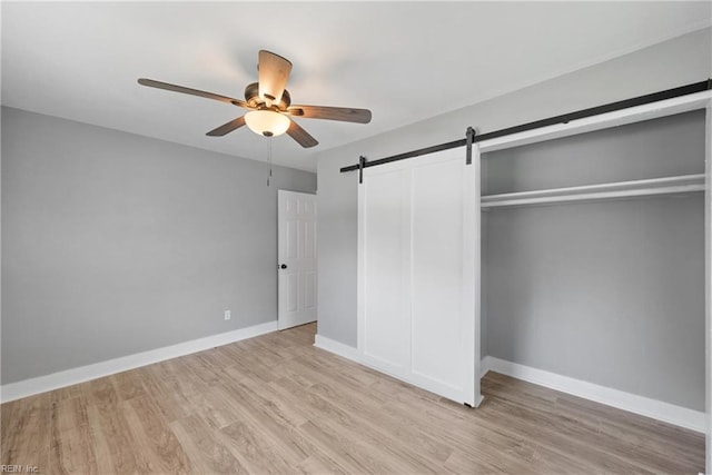 unfurnished bedroom featuring a barn door, a closet, ceiling fan, and light hardwood / wood-style flooring