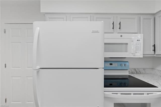 kitchen featuring light stone countertops, white appliances, and white cabinetry