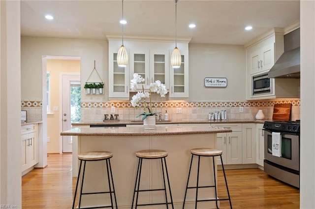 kitchen with a kitchen breakfast bar, wall chimney exhaust hood, light hardwood / wood-style flooring, stainless steel appliances, and white cabinets