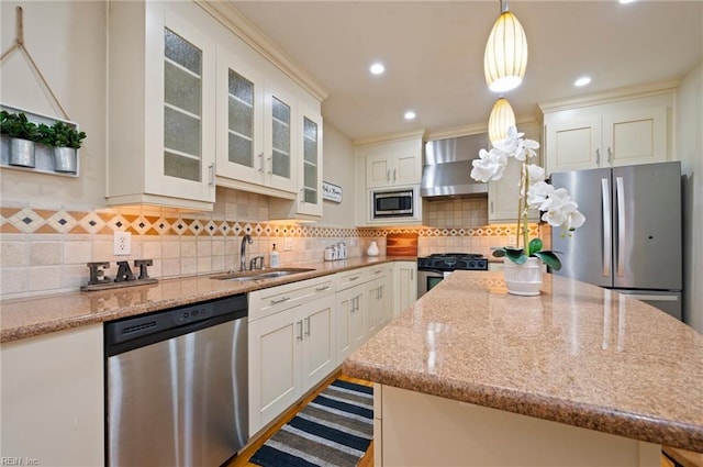 kitchen with wall chimney exhaust hood, pendant lighting, stainless steel appliances, sink, and white cabinets