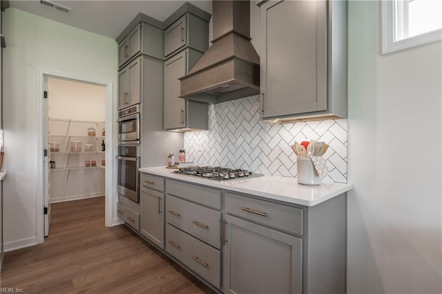 kitchen with gray cabinets, dark wood-type flooring, custom range hood, and stainless steel gas cooktop