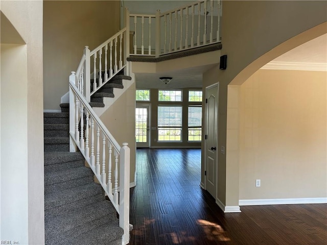 stairway with ornamental molding, hardwood / wood-style floors, and a towering ceiling