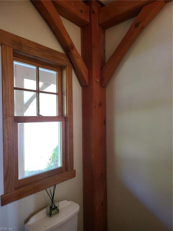 bathroom with beam ceiling, toilet, and plenty of natural light