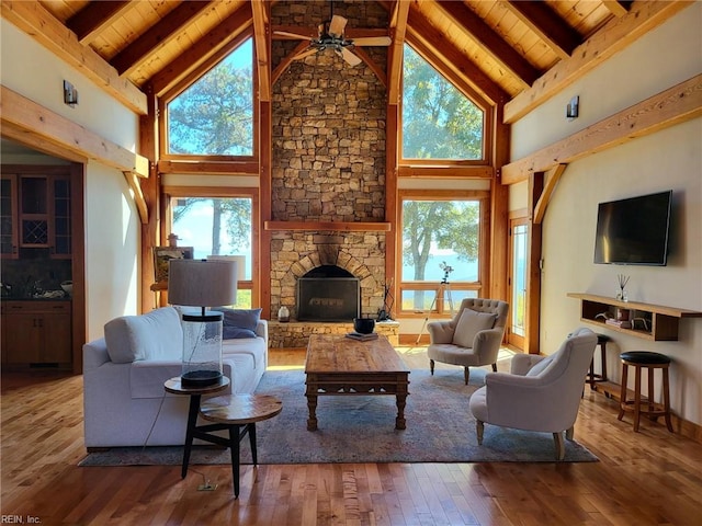 living room featuring hardwood / wood-style flooring, a stone fireplace, ceiling fan, and high vaulted ceiling