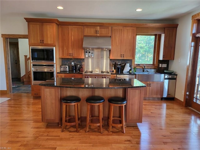 kitchen with light hardwood / wood-style floors, dark stone countertops, stainless steel appliances, a center island, and extractor fan