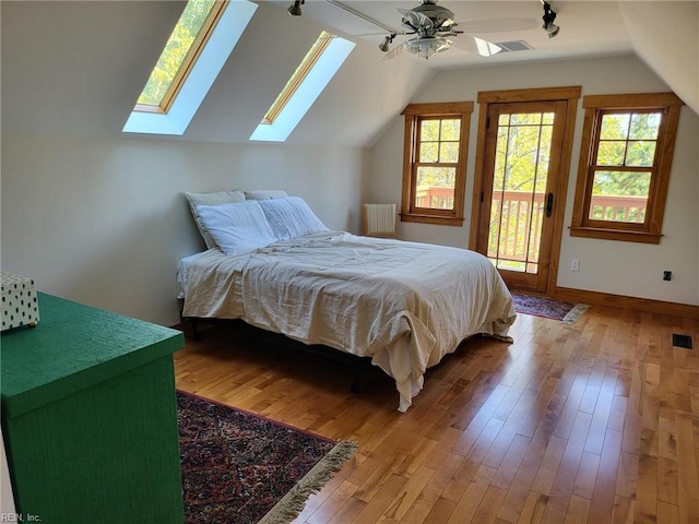 bedroom with radiator heating unit, access to exterior, light wood-type flooring, vaulted ceiling with skylight, and ceiling fan