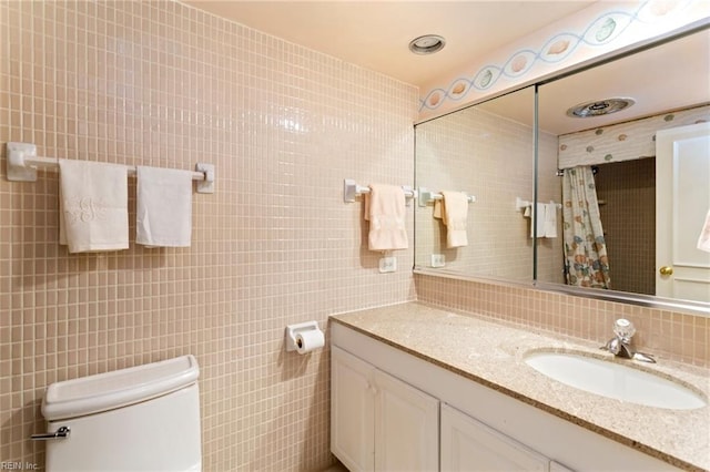 bathroom with tile walls, vanity, toilet, and tasteful backsplash