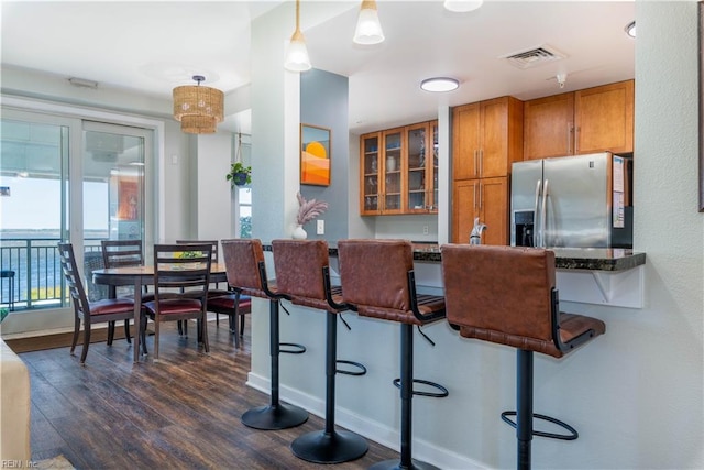 kitchen with a kitchen breakfast bar, dark wood-type flooring, kitchen peninsula, pendant lighting, and stainless steel fridge with ice dispenser