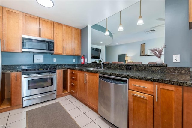 kitchen featuring dark stone counters, light tile patterned flooring, sink, appliances with stainless steel finishes, and decorative light fixtures