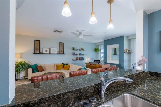 kitchen with dark stone counters, ceiling fan, decorative light fixtures, and sink