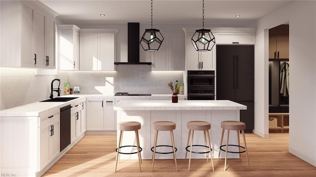 kitchen featuring wall chimney exhaust hood, sink, decorative light fixtures, a center island, and white cabinetry