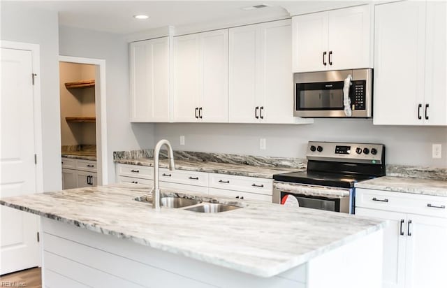 kitchen featuring a kitchen island with sink, sink, white cabinets, and appliances with stainless steel finishes