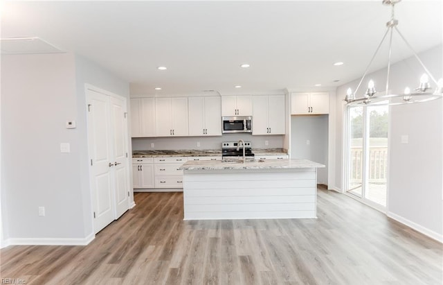 kitchen with appliances with stainless steel finishes, white cabinetry, hanging light fixtures, and an island with sink