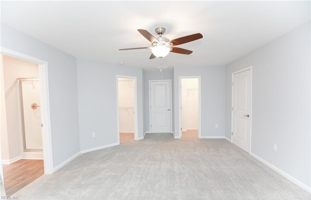 unfurnished bedroom with a walk in closet, ensuite bathroom, ceiling fan, and light carpet