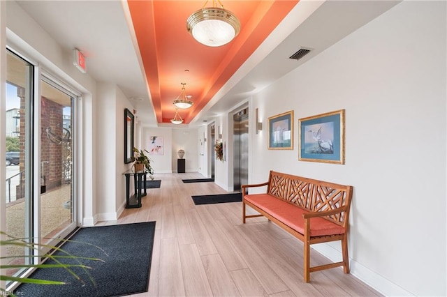 interior space with light wood-type flooring, a raised ceiling, and elevator