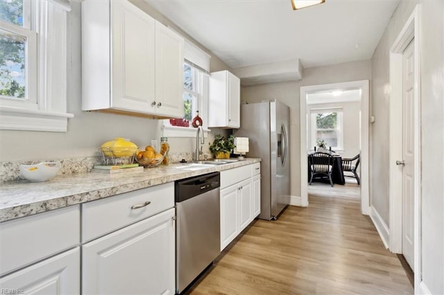 kitchen with appliances with stainless steel finishes, white cabinetry, sink, and light hardwood / wood-style flooring