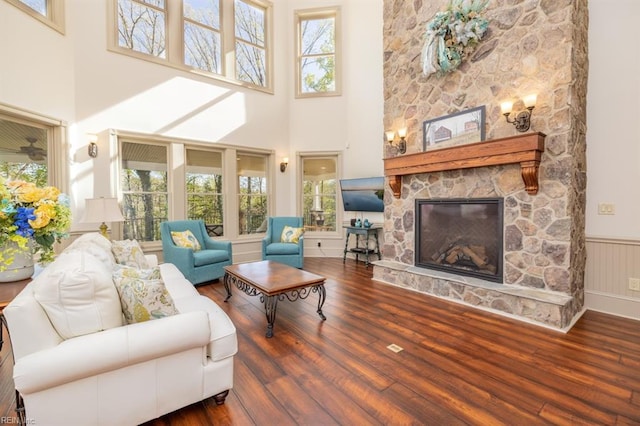 living room with a towering ceiling, hardwood / wood-style floors, a healthy amount of sunlight, and a stone fireplace