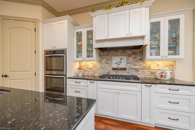 kitchen with appliances with stainless steel finishes, dark stone countertops, ornamental molding, and white cabinets