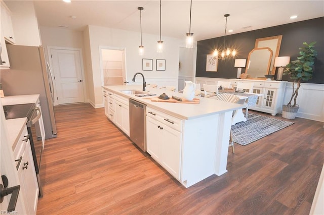 kitchen with wood-type flooring, decorative light fixtures, a center island with sink, white cabinetry, and appliances with stainless steel finishes