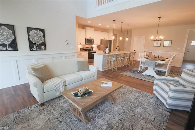 living room with a towering ceiling, a notable chandelier, sink, and dark wood-type flooring